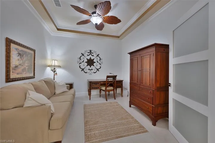 Living room with ornamental molding, light tile patterned flooring, ceiling fan, and a tray ceiling
