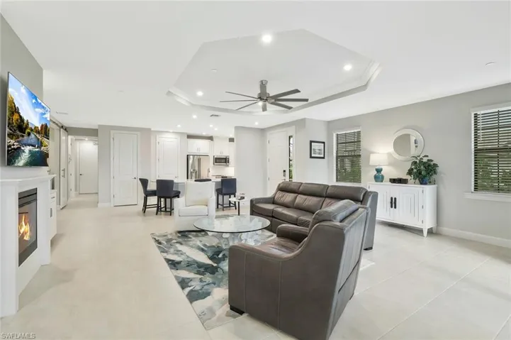Living area featuring recessed lighting, a ceiling fan, a glass covered fireplace, a tray ceiling, and ornamental molding