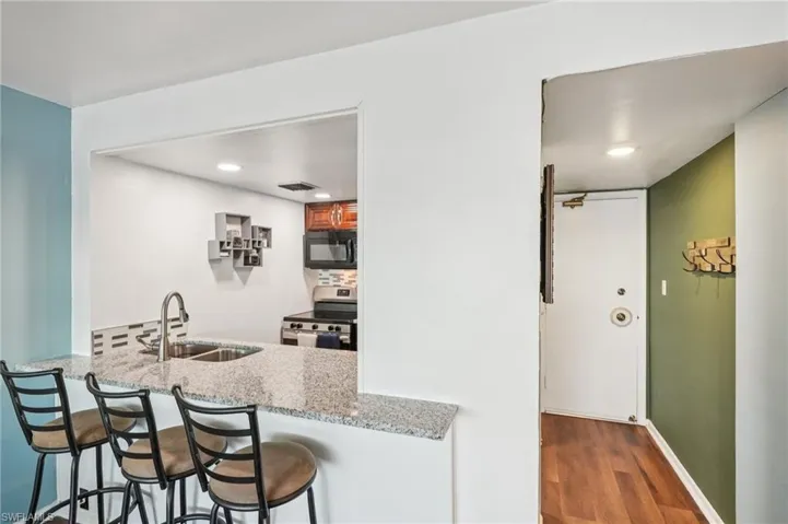 Kitchen featuring stainless steel range, black microwave, a breakfast bar, dark wood-style floors, and light stone counters