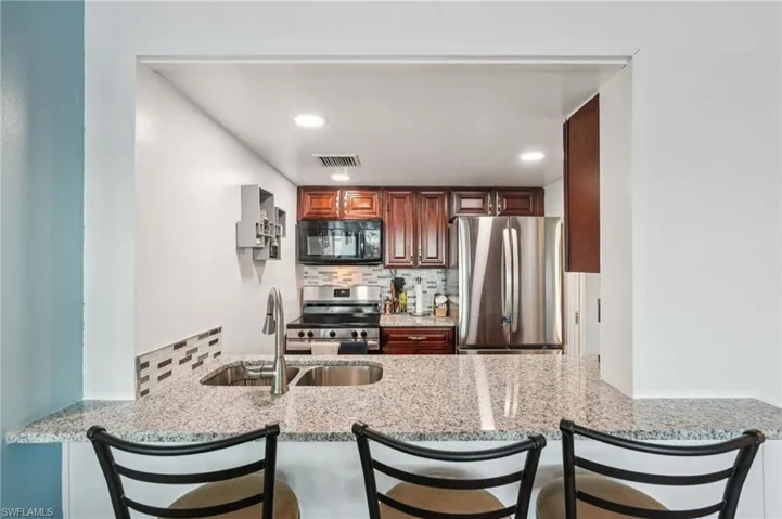 Kitchen featuring stainless steel appliances, tasteful backsplash, a breakfast bar, light stone counters, and recessed lighting