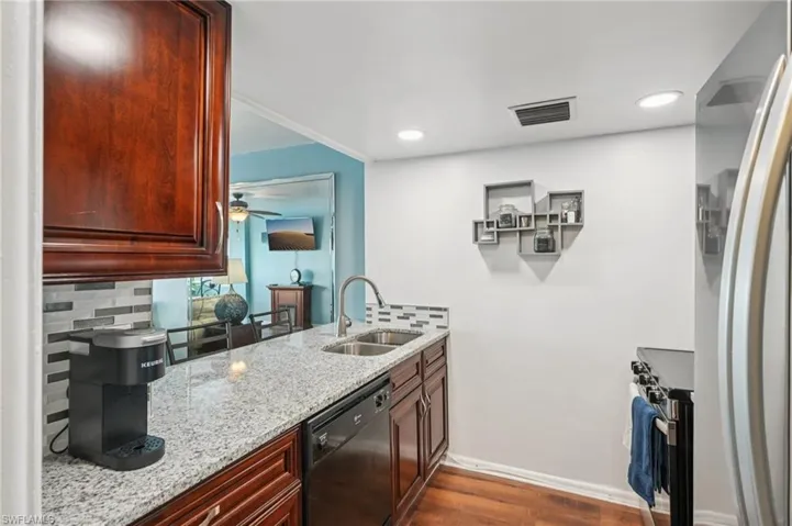 Kitchen featuring freestanding refrigerator, tasteful backsplash, light stone counters, black dishwasher, and stainless steel range with electric stovetop
