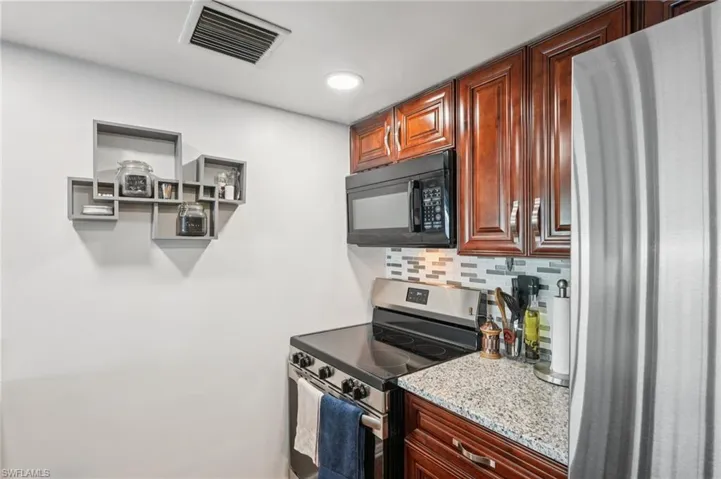 Kitchen featuring appliances with stainless steel finishes, backsplash, light stone counters, and open shelves