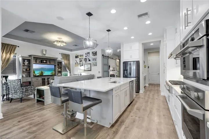Open-concept kitchen with a large central island, light wood-finish flooring, white cabinetry, stainless steel appliances, and recessed lighting