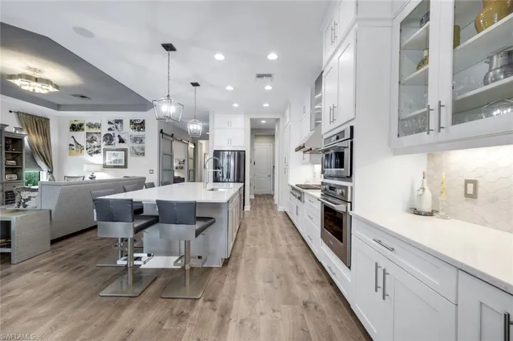 Contemporary kitchen featuring white cabinetry, integrated stainless steel appliances, a center island with seating, pendant lighting, and wood-finish flooring