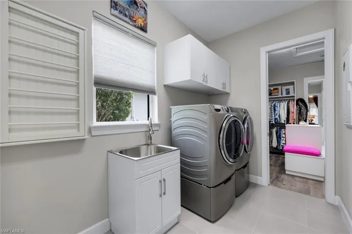 Utility room featuring a built-in folding rack, a window with natural light, a stainless steel utility sink with a white shaker-style cabinet, and white upper cabinetry