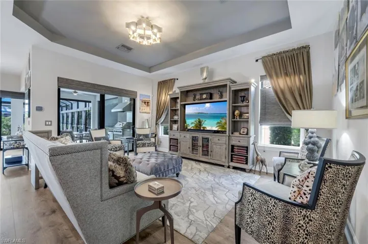 Spacious living area featuring tray ceilings, wood-finish flooring, and a large built-in entertainment center