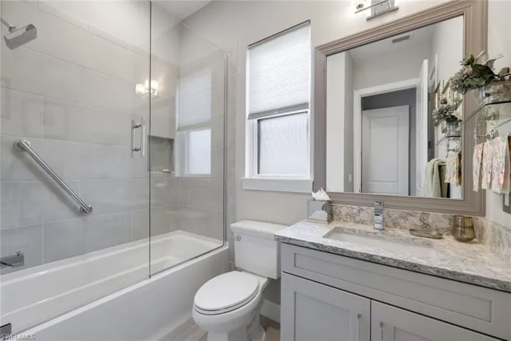 Contemporary bathroom featuring a tub-shower combination with glass enclosure, light gray subway tile surround, and a built-in shower niche