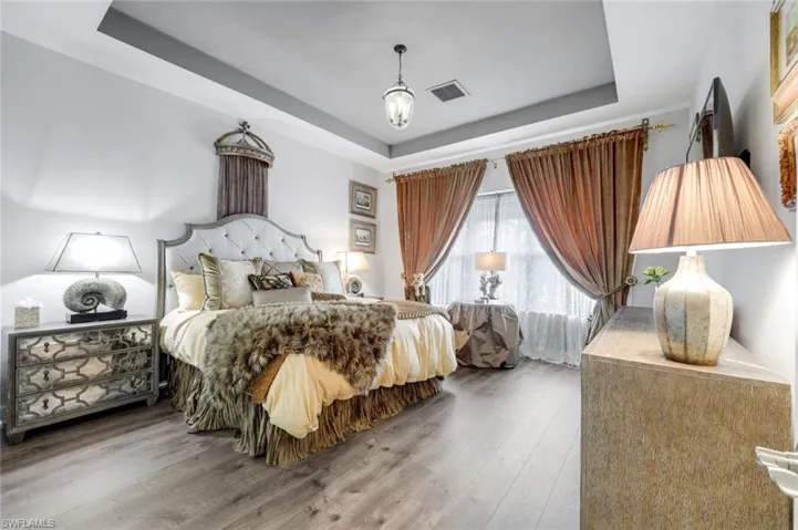 Bedroom featuring wood-finish flooring, a tray ceiling with recessed lighting, and a chandelier