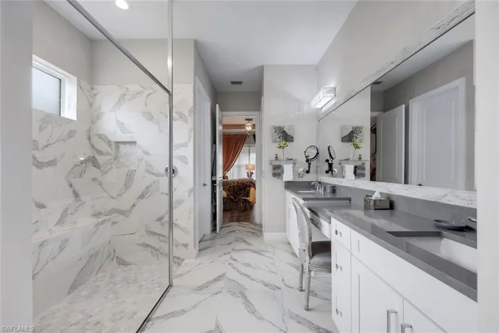 Spacious bath featuring a glass-enclosed shower with a built-in bench, dual vanity with undermount sinks, stone countertops, and full-wall mirror