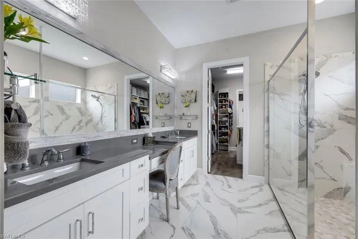 Spacious bathroom featuring marble-look tile flooring and shower surround, a double vanity with grey countertops, and a full-length mirror