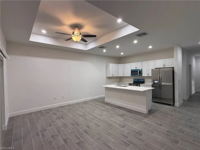 Kitchen with a tray ceiling, appliances with stainless steel finishes, recessed lighting, white cabinets, and open floor plan