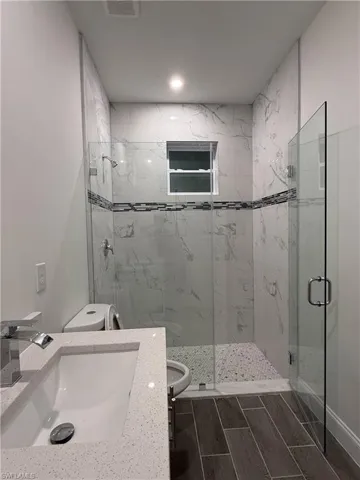 Bathroom with a marble finish shower, wood tiled floors, and vanity