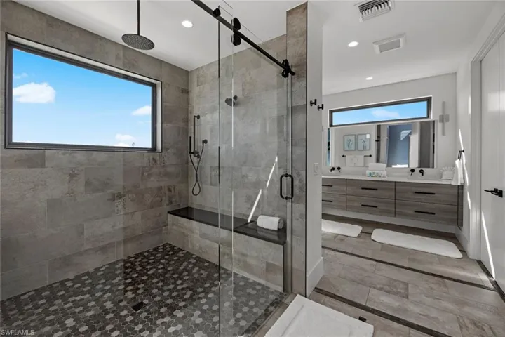 Bathroom featuring a shower with shower door, plenty of natural light, tile floors, and vanity with extensive cabinet space