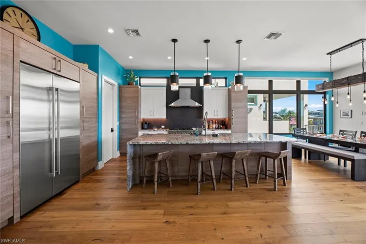 Kitchen with an island with sink, hardwood / wood-style flooring, stainless steel built in refrigerator, decorative light fixtures, and tasteful backsplash