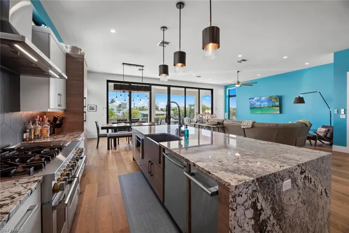 Kitchen featuring a center island with sink, stainless steel appliances, hanging light fixtures, wall exhaust hood, and wood flooring