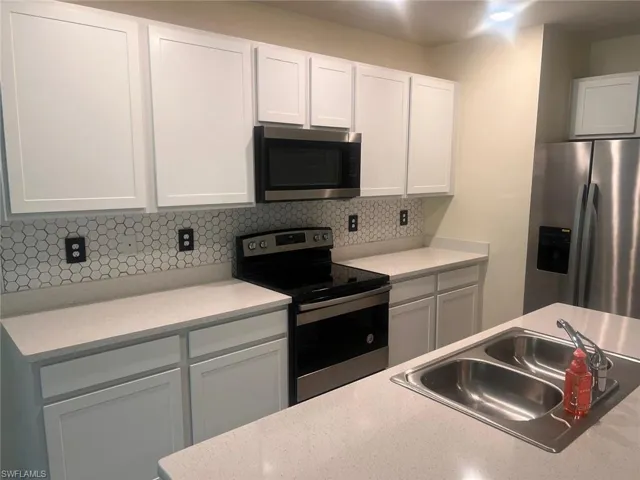 Kitchen featuring appliances with stainless steel finishes, white cabinetry, and backsplash