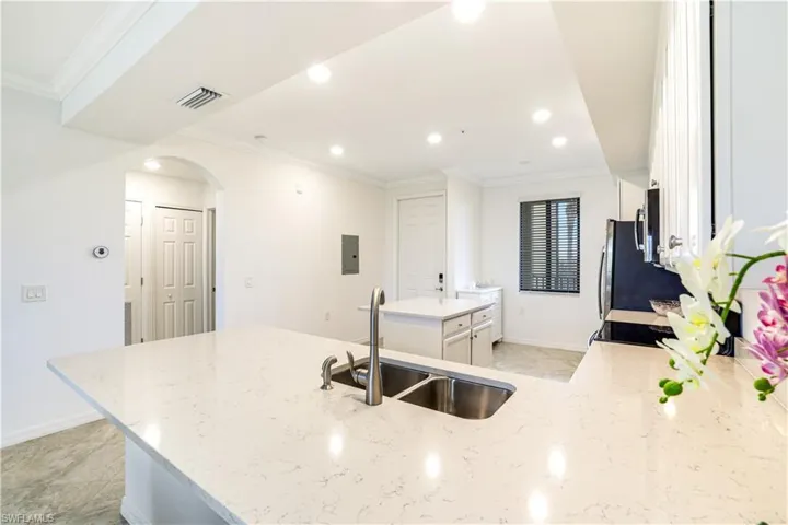 Kitchen featuring a peninsula, ornamental molding, white cabinetry, a kitchen island, and arched walkways