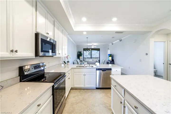 Kitchen with stainless steel appliances, arched walkways, white cabinets, open floor plan, and ornamental molding