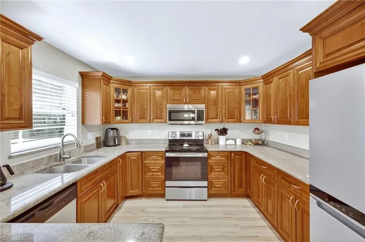Kitchen with stainless steel appliances, brown cabinetry, light stone countertops, light wood finished floors, and recessed lighting
