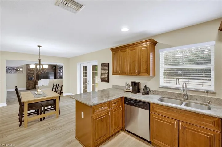 Kitchen with stainless steel dishwasher, brown cabinets, a peninsula, a chandelier, and light stone counters