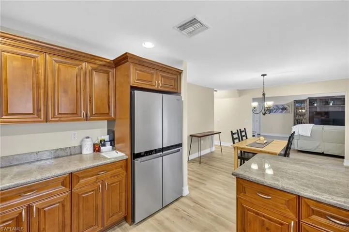 Kitchen with freestanding refrigerator, brown cabinetry, light wood-type flooring, pendant lighting, and light stone countertops