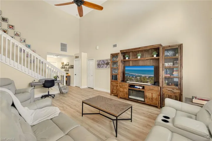 Living room featuring high vaulted ceiling, stairway, light wood-style floors, and ceiling fan