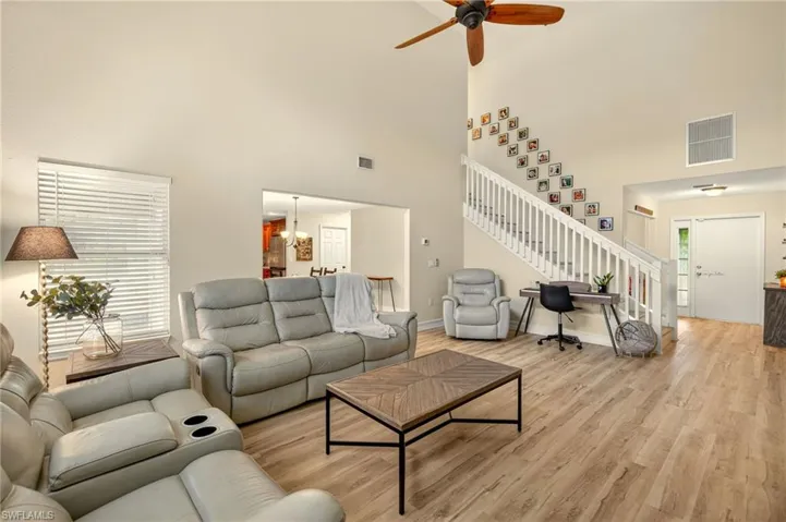Living room featuring a high ceiling, stairway, ceiling fan, and light wood-style flooring