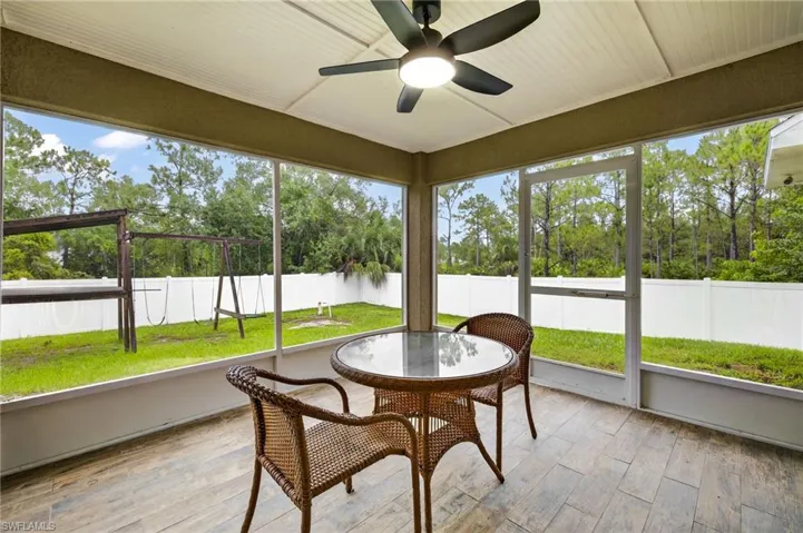 Sunroom with ceiling fan, outdoor dining space, and view of scattered trees