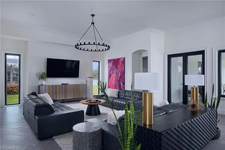 Spacious living area featuring herringbone-patterned flooring, a large wall-mounted television, and a contemporary circular chandelier