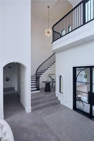 Grand foyer featuring a curved staircase with black wrought iron balusters, a double-height ceiling, and a contemporary chandelier