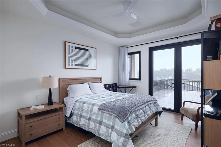 Hardwood flooring and a tray ceiling with crown molding define this space, featuring large glass doors that open to an exterior balcony with black railings