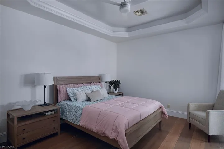 Spacious room with tray ceiling and crown molding, featuring wood-finish flooring, a ceiling fan, and baseboards