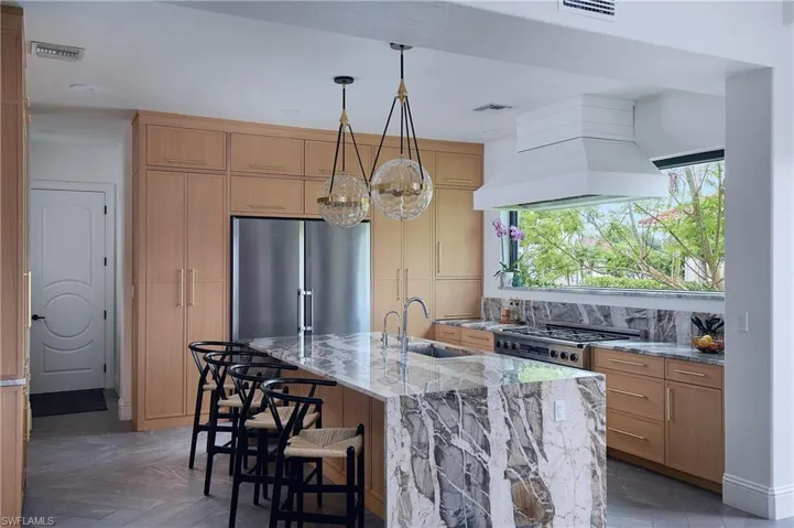 Kitchen featuring a waterfall island with marble countertop, wood-finish cabinetry, stainless steel refrigerator, and recessed lighting