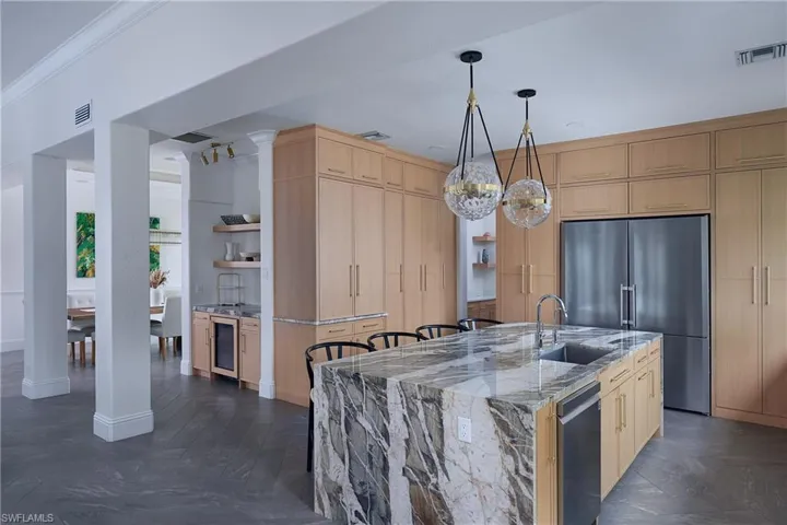 Gourmet kitchen featuring a waterfall island with integrated sink, stainless steel appliances, extensive wood cabinetry, and pendant lighting