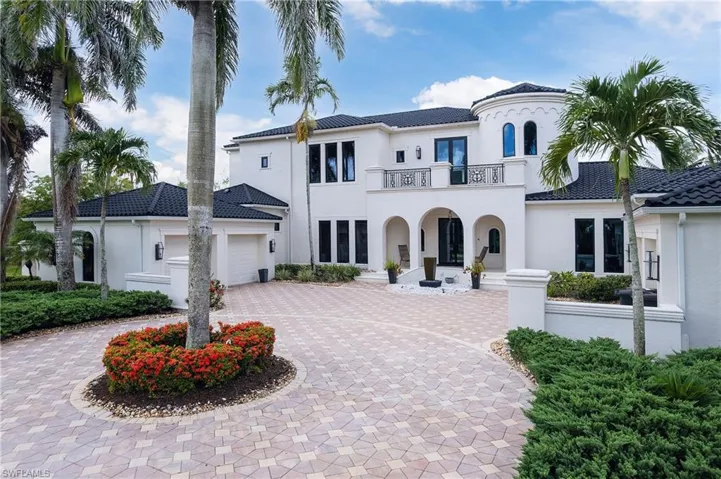 Stucco exterior residence with a tiled roof, featuring a paver driveway, multiple garage doors, and a second-story balcony with iron railings