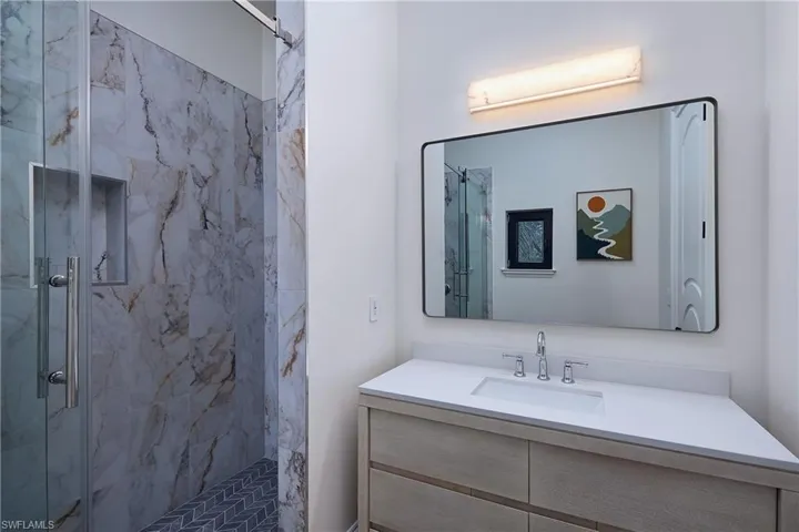 Modern bathroom featuring a glass-enclosed shower with marble-style wall tiling and a herringbone-patterned floor