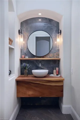 Arched vanity niche featuring a floating wood-finish vanity, vessel sink, and stone-accent wall