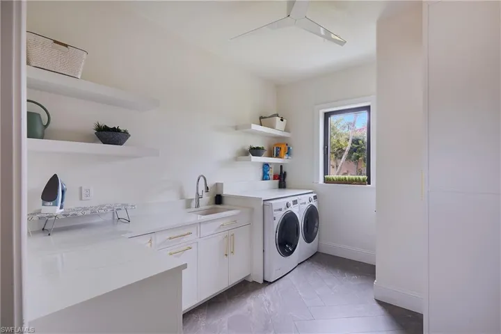 Dedicated laundry room featuring a utility sink with a chrome faucet, white cabinetry with gold-tone hardware, and white countertops