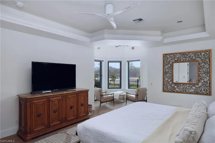 Room featuring large bay windows overlooking a water feature, crown molding, a tray ceiling, and a modern ceiling fan