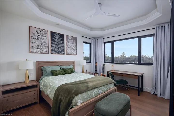 Tray ceiling with crown molding, black-framed windows, hard surface flooring, and a ceiling fan