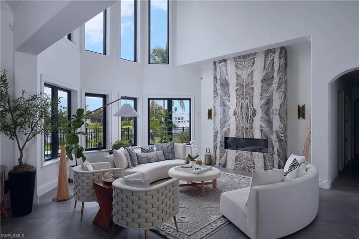 Vaulted ceiling living area featuring a full-height decorative stone fireplace, wide plank wood-finish flooring, and multiple floor-to-ceiling windows