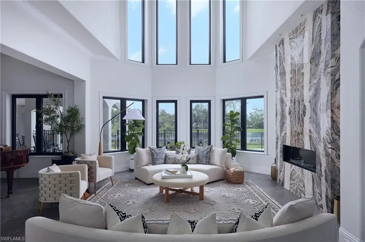 Contemporary living area featuring a two-story ceiling, multiple large windows with black frames, a statement fireplace with a stone-finish facade, and recessed ceiling lights