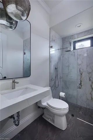 Modern bathroom featuring a walk-in shower with a glass enclosure, marble-style wall tiling, and dark-toned floor tiling