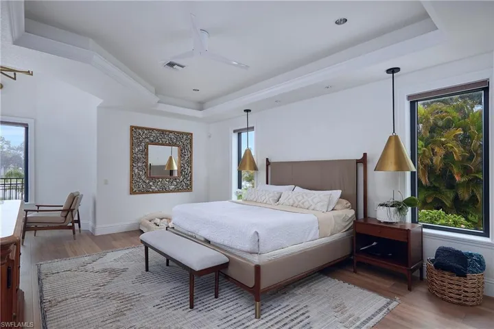Bedroom featuring tray ceilings, recessed lighting, wood-finish flooring, and large windows with exterior foliage visible