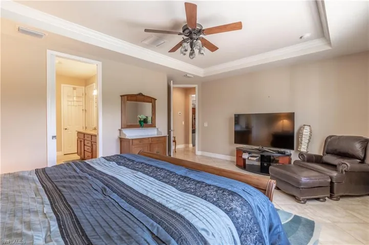 Tiled bedroom with ensuite bathroom, a tray ceiling, ceiling fan, and ornamental molding