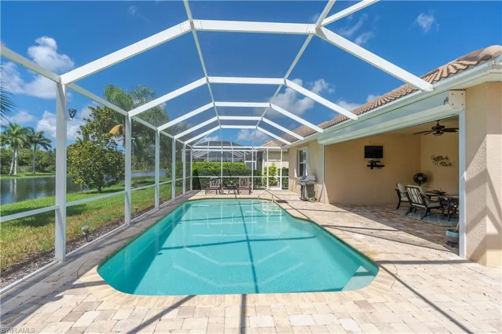 View of swimming pool featuring a patio, a water view, ceiling fan, and glass enclosure