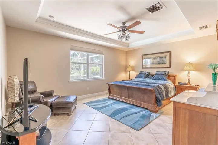 Tiled bedroom featuring a raised ceiling and ceiling fan
