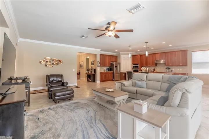 Living room featuring ceiling fan, ornamental molding, and light tile patterned floors