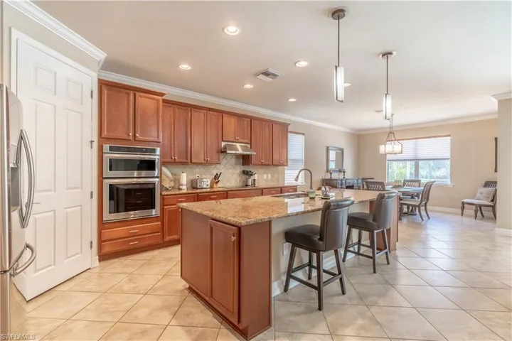 Kitchen featuring light stone countertops, hanging light fixtures, appliances with stainless steel finishes, decorative backsplash, and a center island with sink