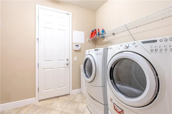 Washroom with washing machine and clothes dryer and light tile patterned floors